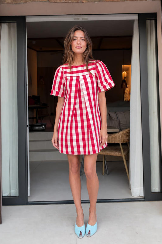 Front view of woman wearing red gingham check pleated mini dress with light blue heels