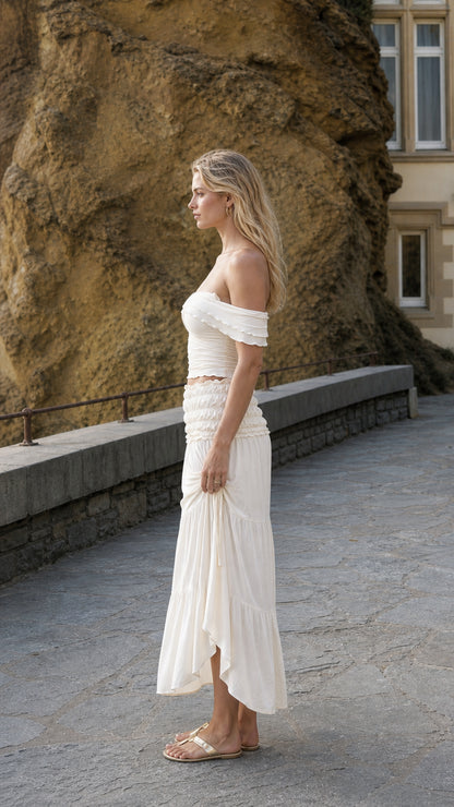 Side profile view of woman in ivory two-piece set standing near stone wall
