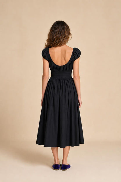 Back view of woman in black smocked midi dress against neutral background
