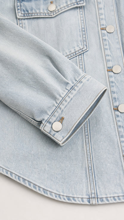 Close-up detail of light blue denim shirt jacket sleeve cuff and pocket