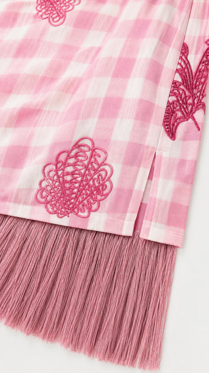 Close-up of pink gingham fabric, embroidery, and fringe hem detail