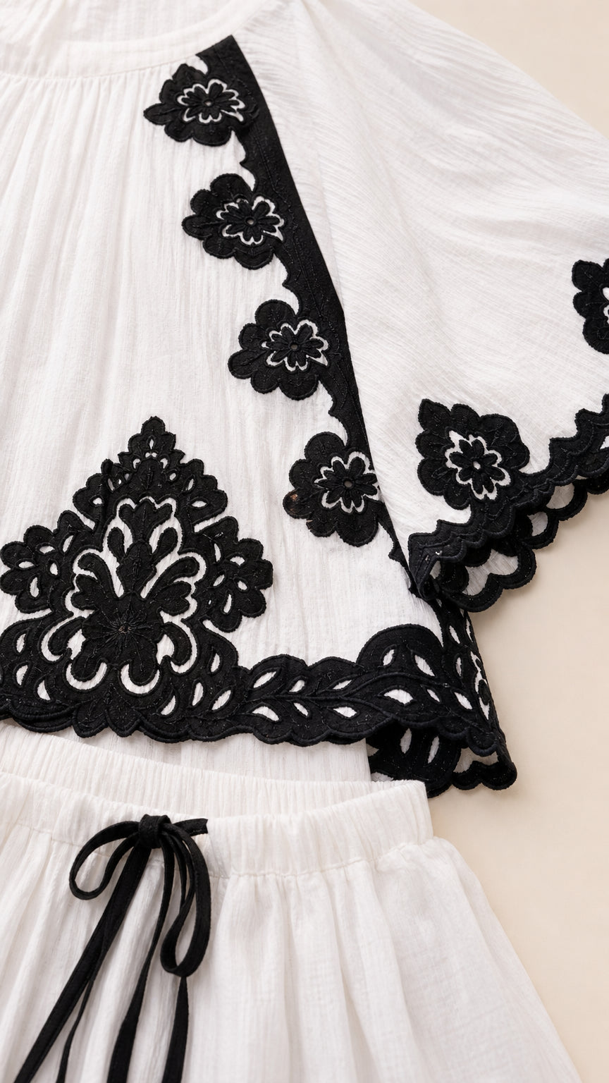 Close-up detail of black embroidery on white cape top and skirt waistband