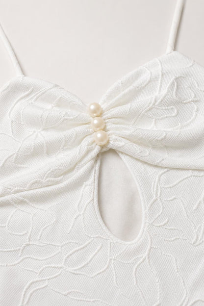 Close-up detail of bodice cutout and faux pearl buttons on white dress