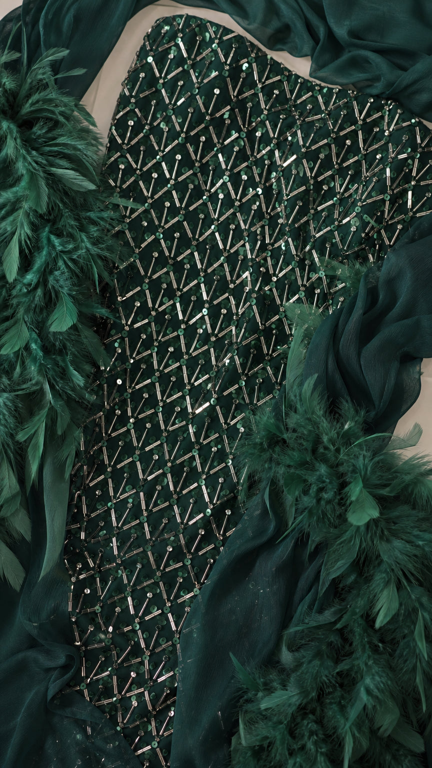Close up fabric detail of emerald green sequins and feather trim