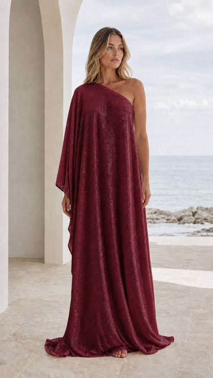 Front view of woman wearing burgundy one-shoulder draped maxi kaftan dress