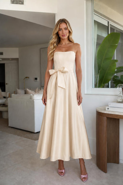 Model wearing champagne strapless bow waist midi dress